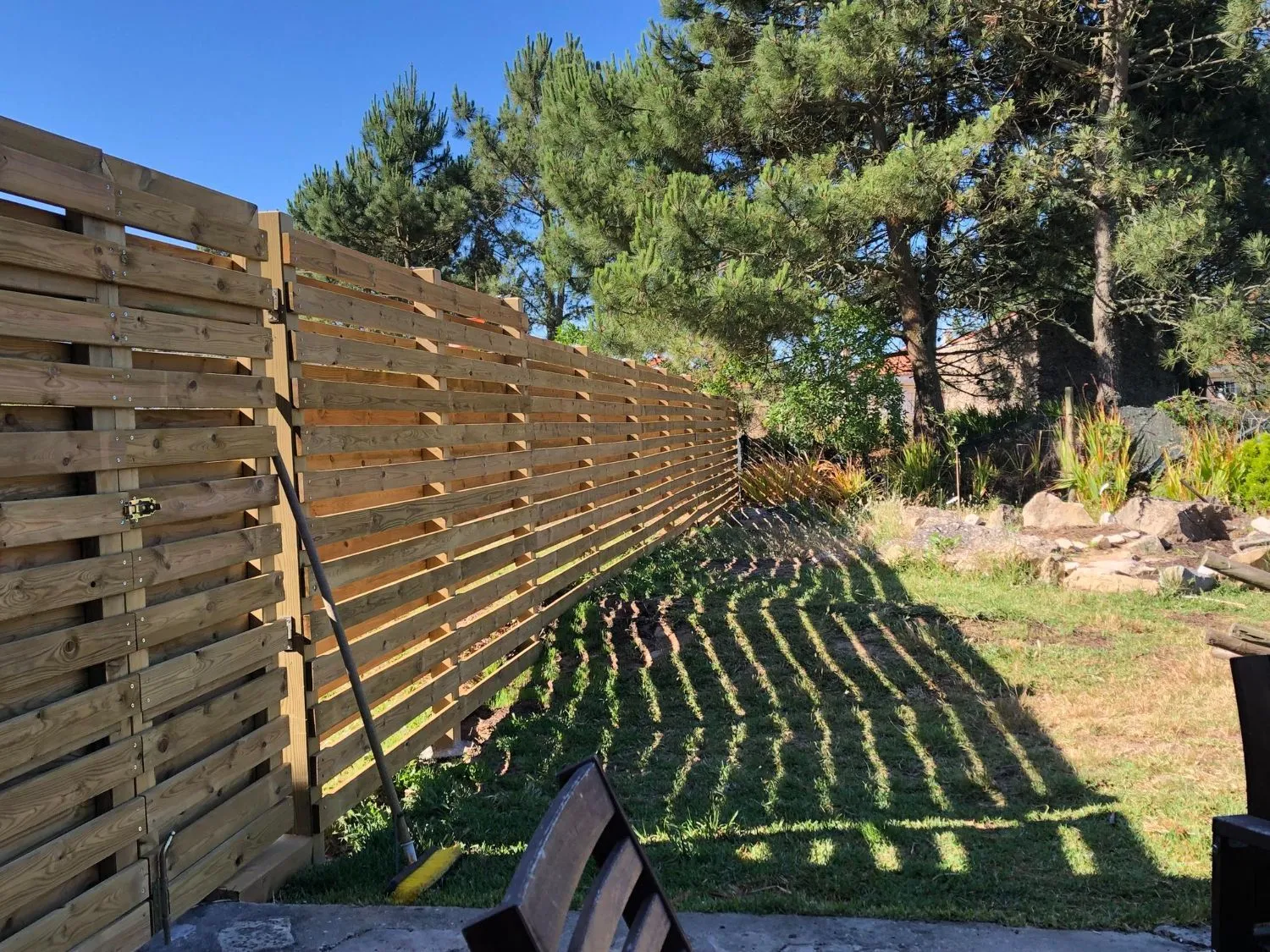A long wooden fence runs alongside a landscaped garden bed.