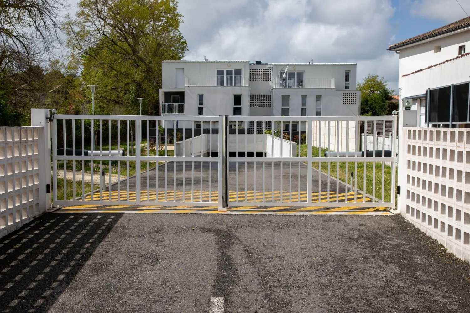 Double metal gate across the paved entrance to a white apartment building