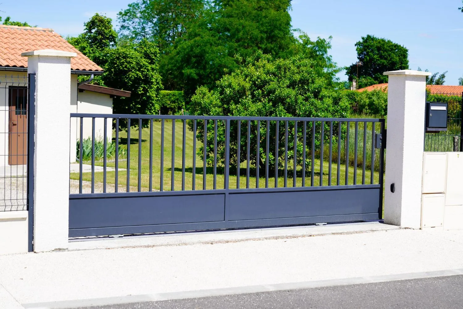Gray aluminum sliding driveway gate between white pillars