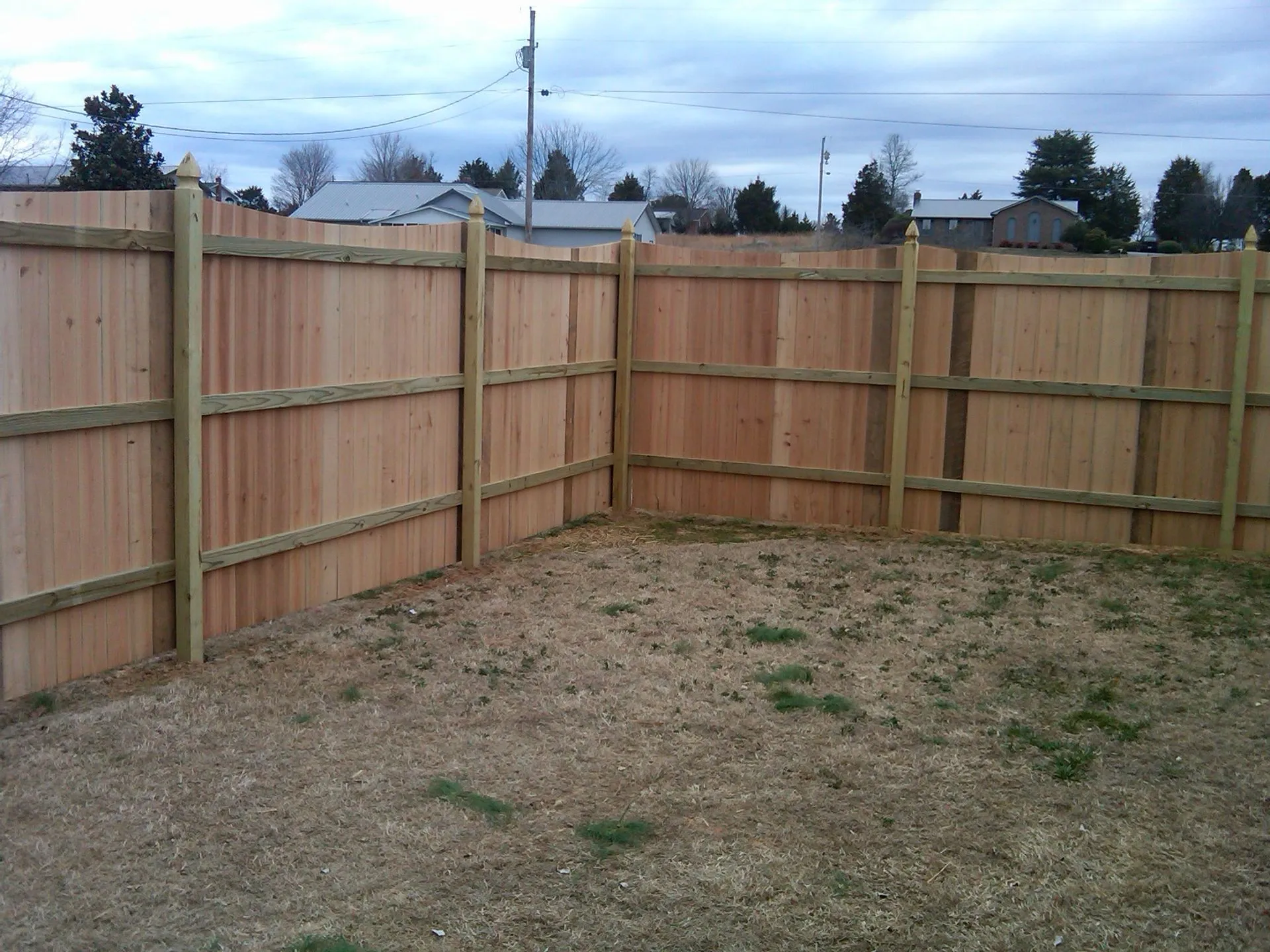 A wood privacy fence surrounds a grassy area in a backyard