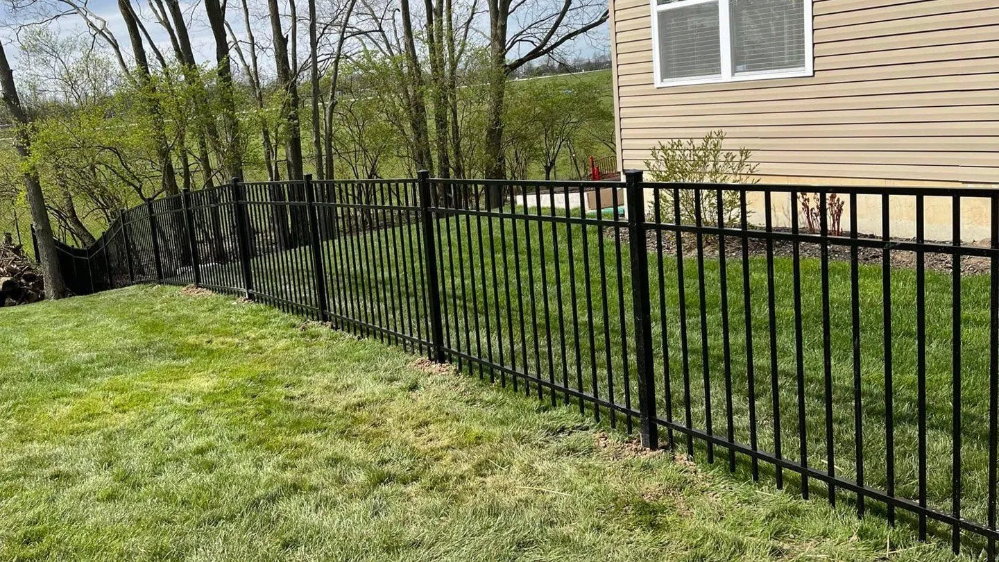 Black ornamental aluminum fence along a sloped lawn beside a house