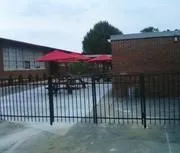 Black ornamental fence enclosing a patio with red umbrellas beside a brick building