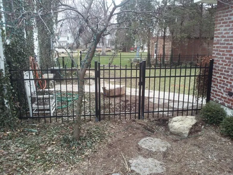 A black steel fence surrounds a backyard with a brick building in the background.