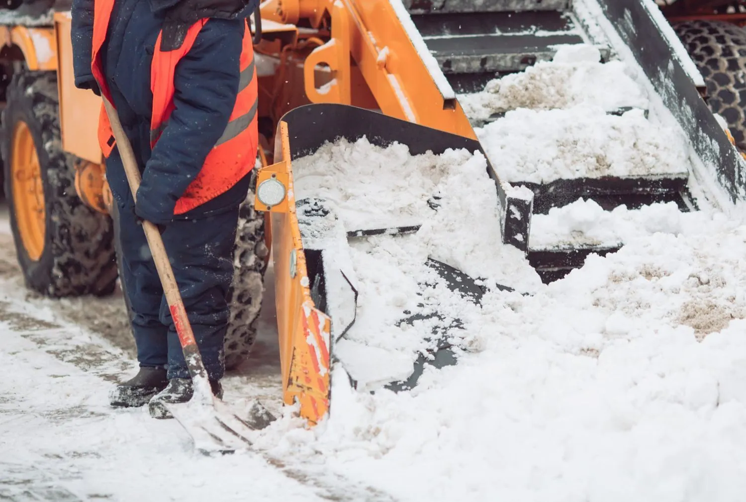 Skid steer pushing snow while a worker shovels a driveway
