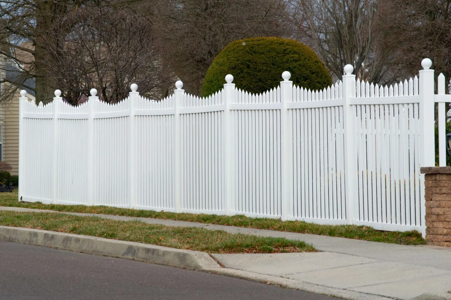 White scalloped vinyl picket fence along a sidewalk