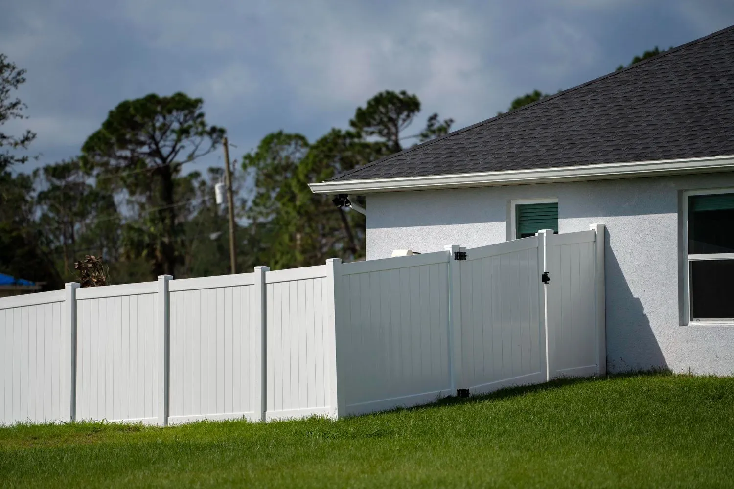 White vinyl privacy fence and gate beside a gray house