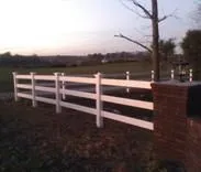 White three-rail fence running out from a brick pillar at dusk