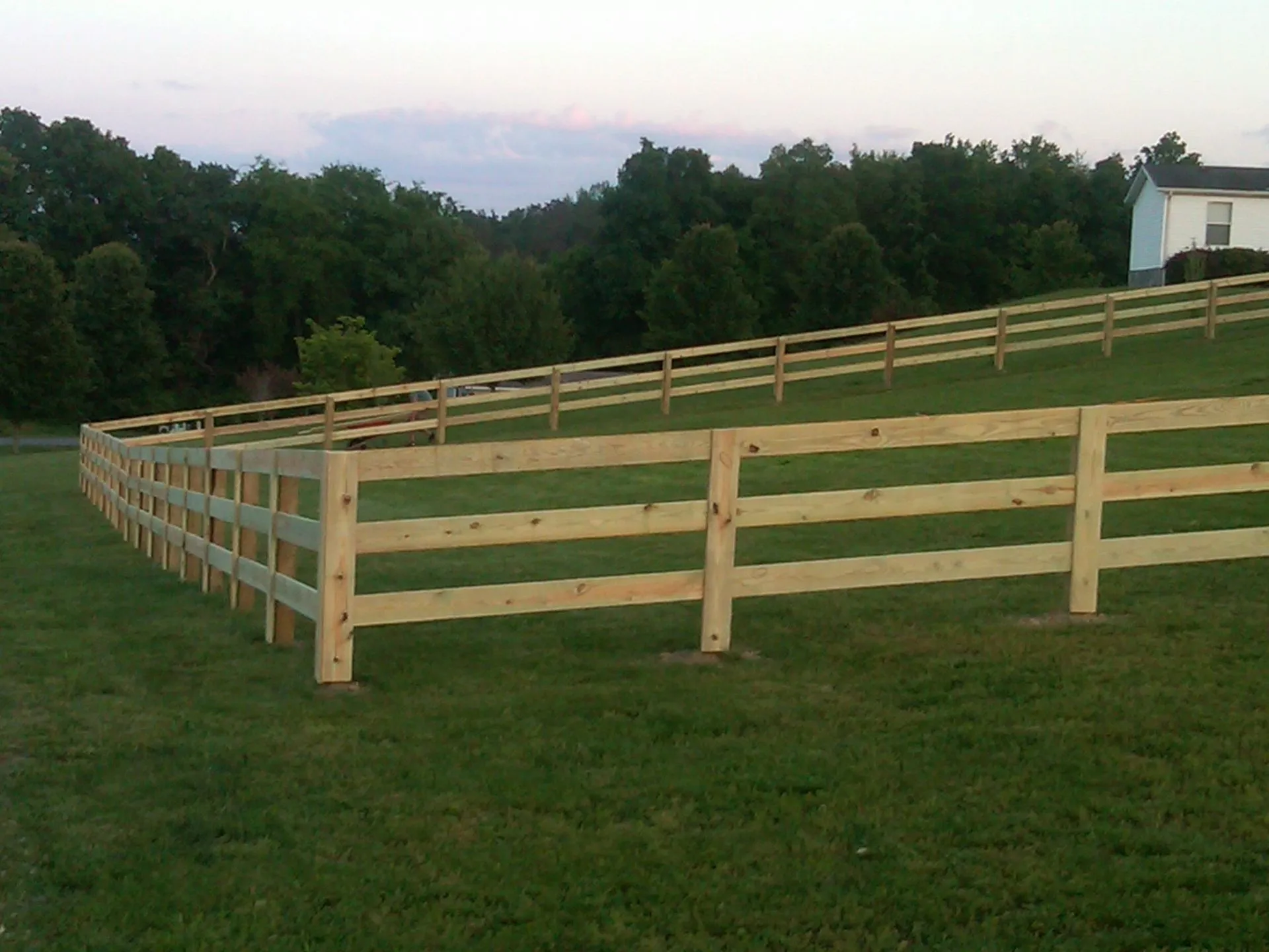 Three-rail wood board fence enclosing a grassy field at dusk