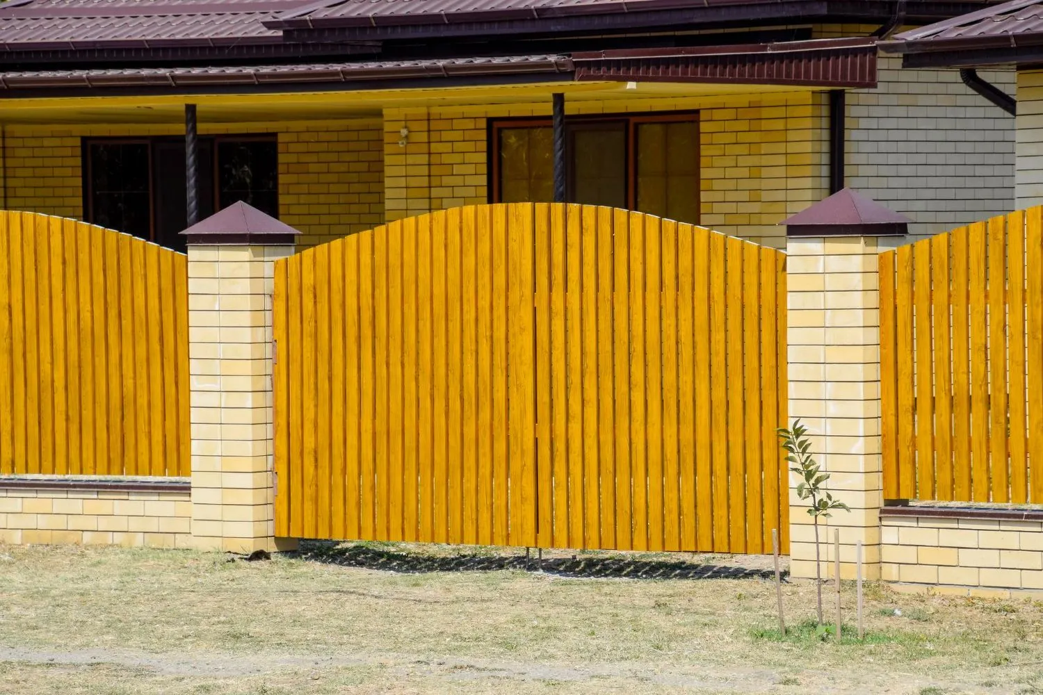Tall yellow wood privacy fence and gate between brick pillars