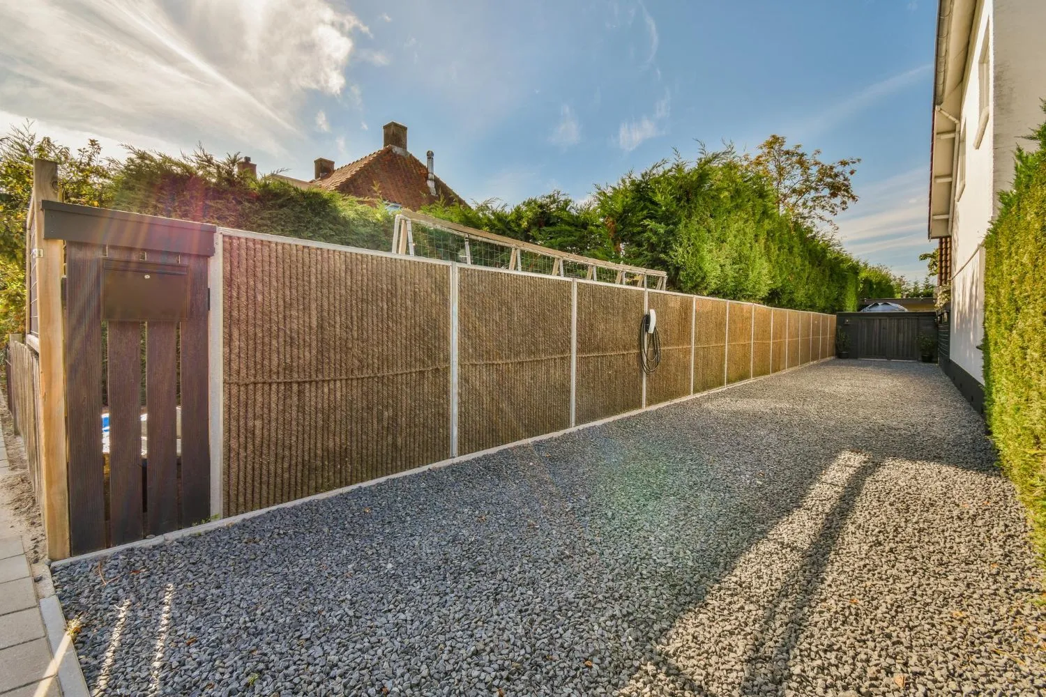 Tall wood privacy fence and gate lining a gravel driveway