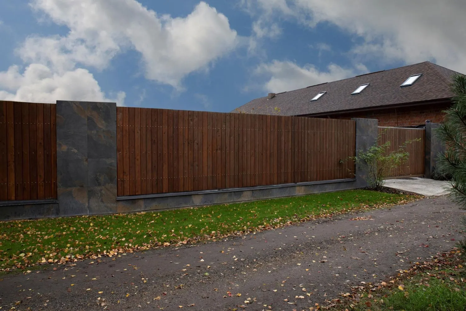 Dark stained wood privacy fence with stone pillars along a driveway